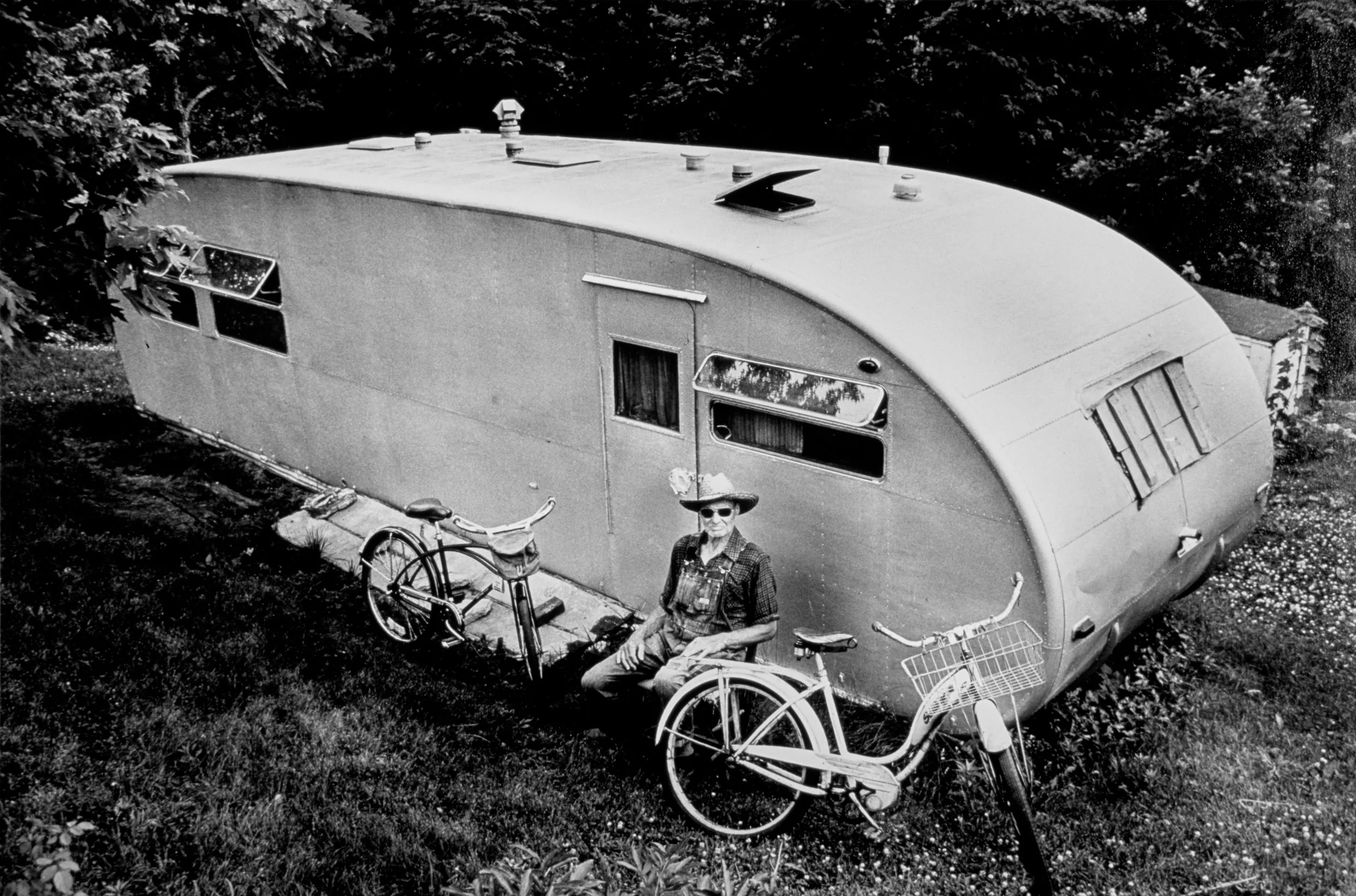 Still Peddling — George Swope, 80, sits alongside his 1952 silver camping trailer he calls home, with his bicycles nearby, in Rocheport, Missouri during the summer of 1978. For 50 years Swope rode his old Schwinn bicycle throughout the Midwest and West working as a itinerant migrant farm worker. “I had plenty of nerve and I ain’t afraid of noth’in,” he says about his time peddling his bicycle to and from places like Montana, Minnesota and Kansas. His bicycles remain his only mode of transportation.  (Photo by Stephan Savoia)  Published In The Columbia Missourian