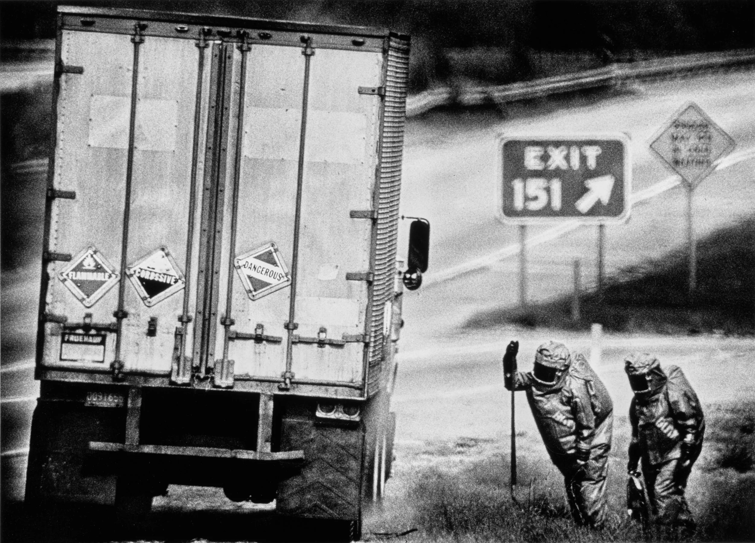 Slow Leak — Two members of the Louisiana State Police Hazardous Materials Response team approach a tractor-trailer leaking a toxic liquid on a highway outside of Baton Rouge, Louisiana. Circa Mid 1980s.  (Photo by Stephan Savoia)  © Stephan Savoia