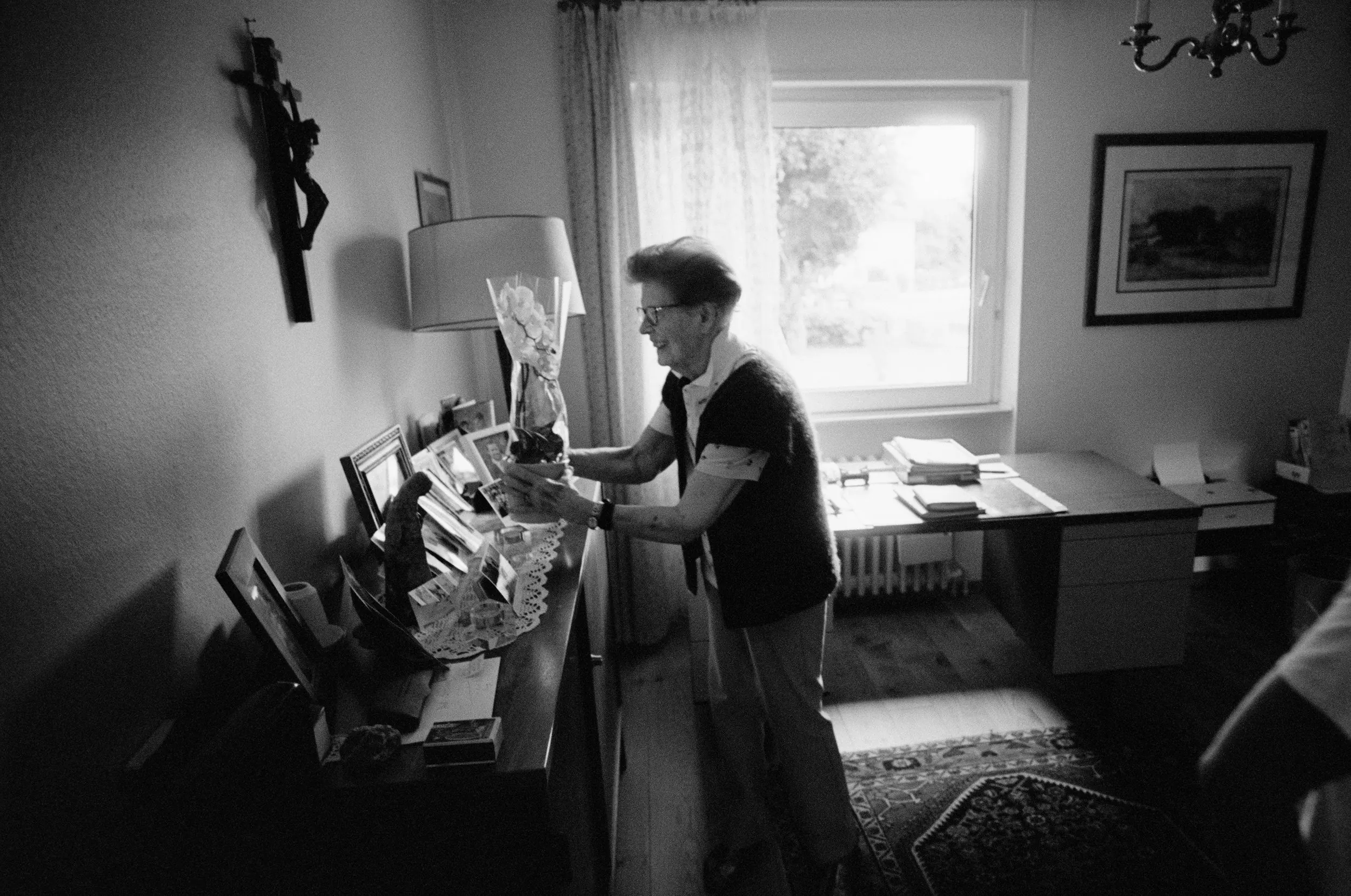 An Alsatian Woman — Ninety-two year old Marie-Thérèse Blanck places an orchid among family photos and religious iconography atop her home's piano in Thann, France in August 2019. Marie-Thérèse was born in Alsace, the most northeastern region of France. Nearly all of the Alsatian border abuts Germany. As Germany began its 1940 annexation of Alsace, Marie-Thérèse was a young teenager whose family sent her to the Landes region of France, farther from the German boarder. While Germany was still occupying Alsace, Marie-Thérèse returned to her Alsatian birthplace and hometown of Brinkheim, France, where she lived most of her young life, before moving to Paris with a Catholic women's group. After Paris, Marie-Thérèse returned again to her beloved Alsace where she married and lived for the rest of her life.  (Photo by Stephan Savoia)  © Stephan Savoia