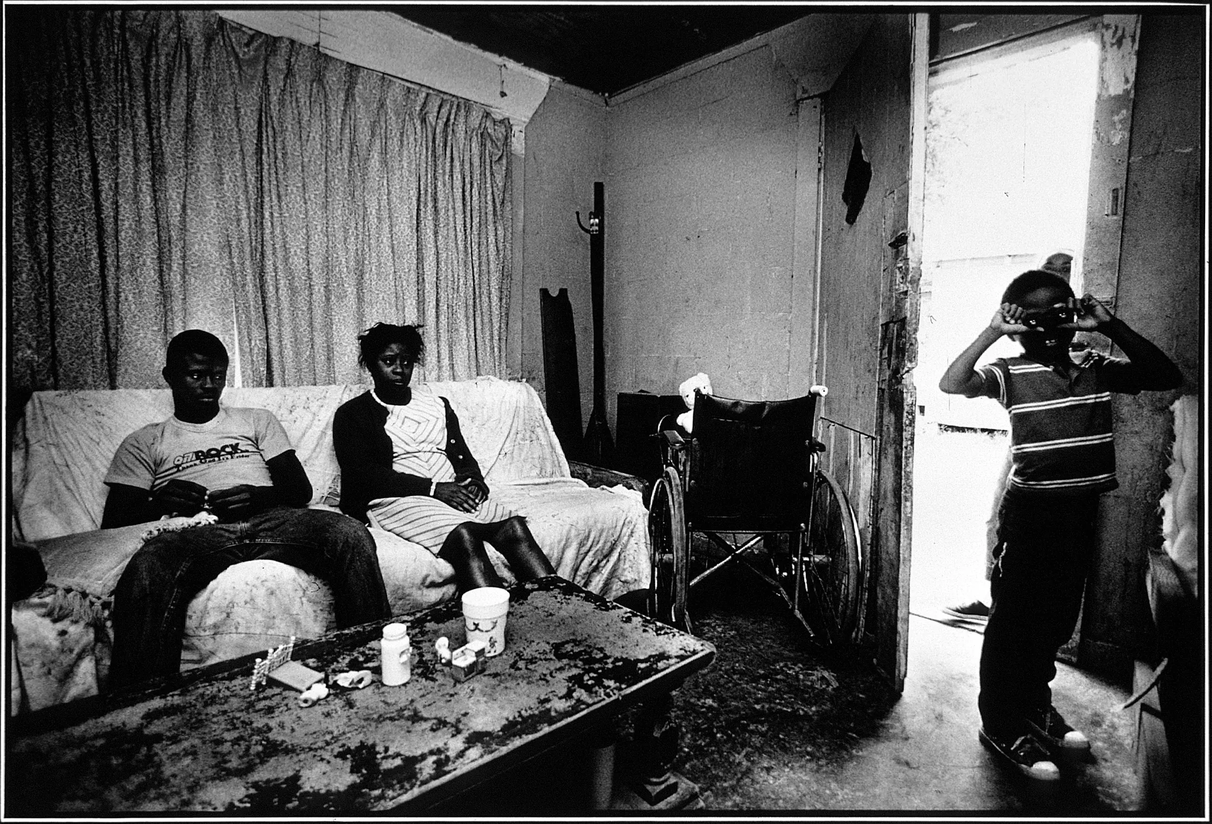 Students at Risk — Louisiana high school senior Richard Cavalier, left, sits on a couch with his handicapped mother Rosa, who was paralyzed after suffering a stroke four years earlier, watching television as her younger son Brian, 7, peers through toy binoculars in their Baton Rouge, Louisiana home.  (Photo by Stephan Savoia)  Published by The Baton Rouge Louisiana State-Times & Morning Advocate on May 16, 1989