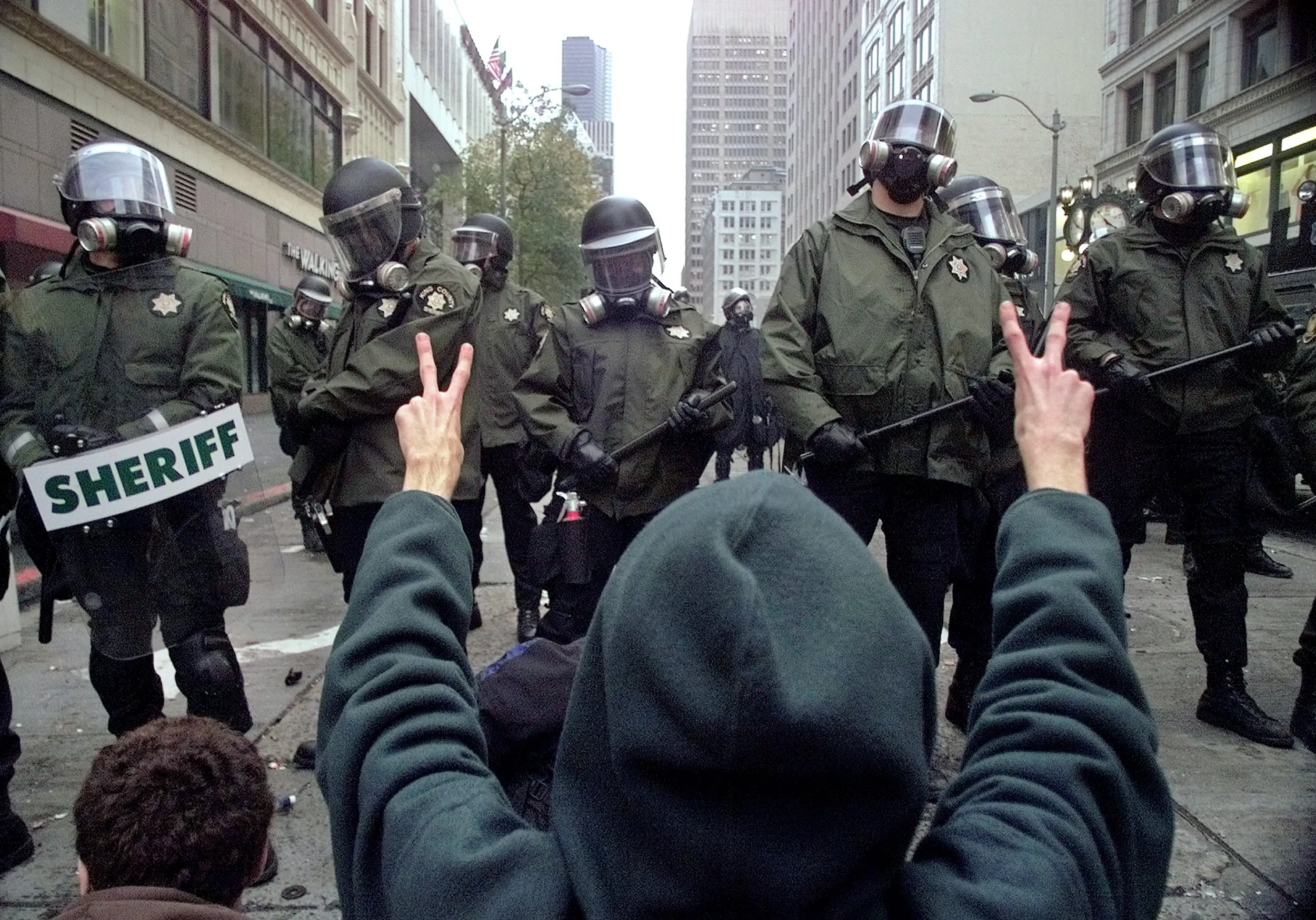 The Battle In Seattle — A World Trade Organization protestor confronts riot police from the sheriff's department with peace signs during a standoff at a downtown Seattle, Washington intersection as WTO protests began on Tuesday afternoon, November 30, 1999. WTO protests continued throughout the week, clogging city streets and crippling the WTO conference.  (AP Photo/Stephan Savoia)  © The Associated Press
