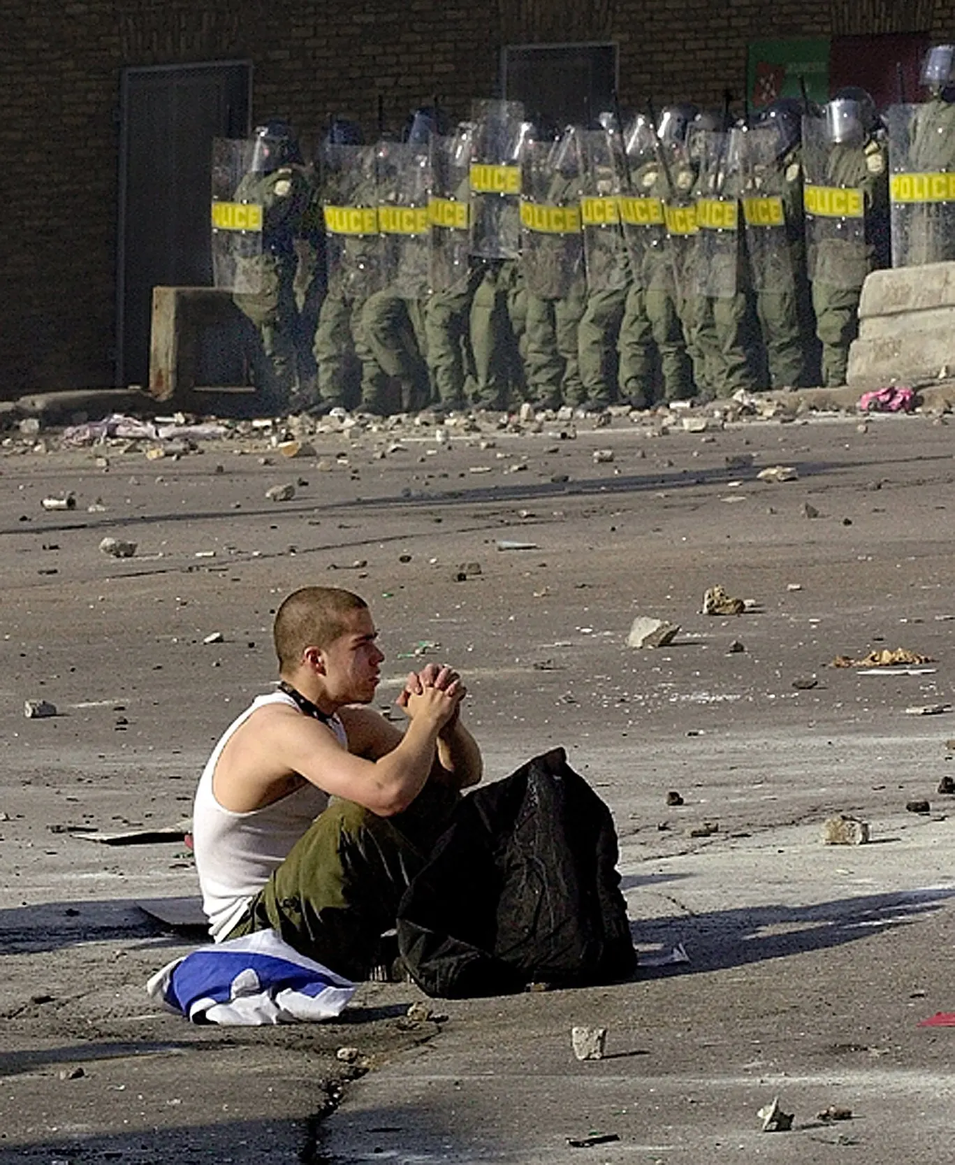 Protester Meditation — A protester claps his hands together as he sits on a rock-strewn street near a gate in the security fence surrounding the Summit of the Americas in Quebec City, Canada, on Saturday afternoon, April 21, 2001. Confrontations between police and protesters continued for a second day while 34 heads of state from the western hemisphere gathered to discuss the possibility of creating the world's largest free trade zone.  (AP Photo/Stephan Savoia)  © The Associated Press